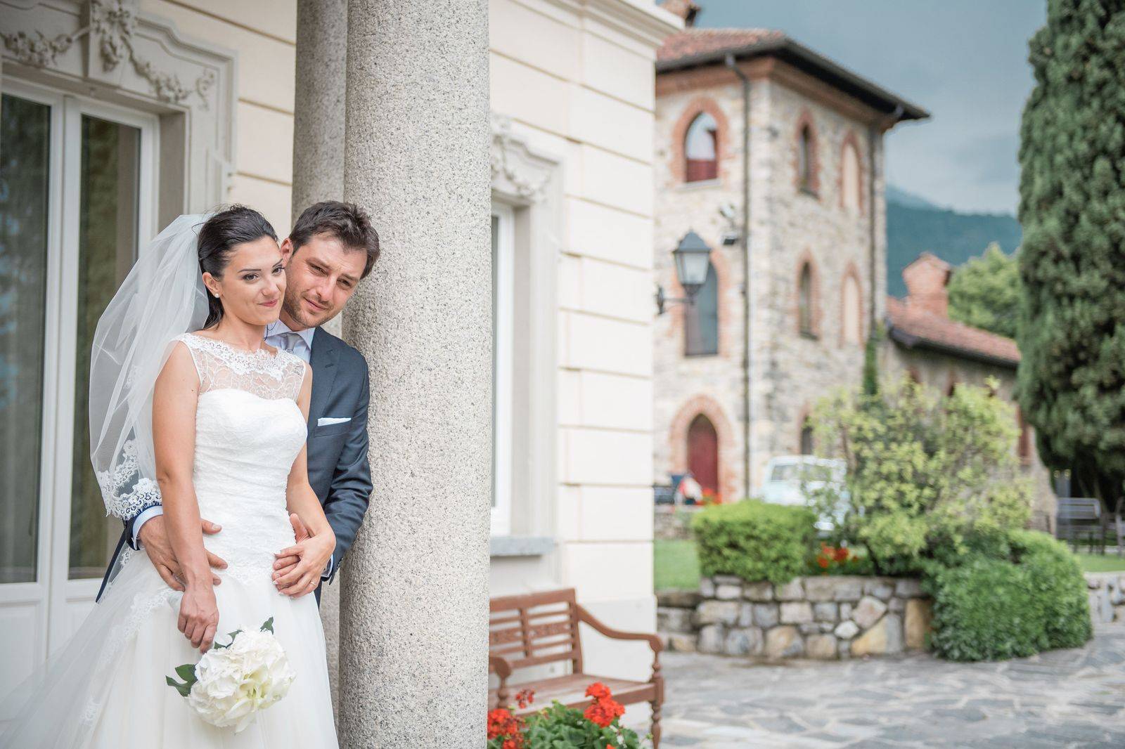 A wedding couple beside a black limousine in front of a stone castle
