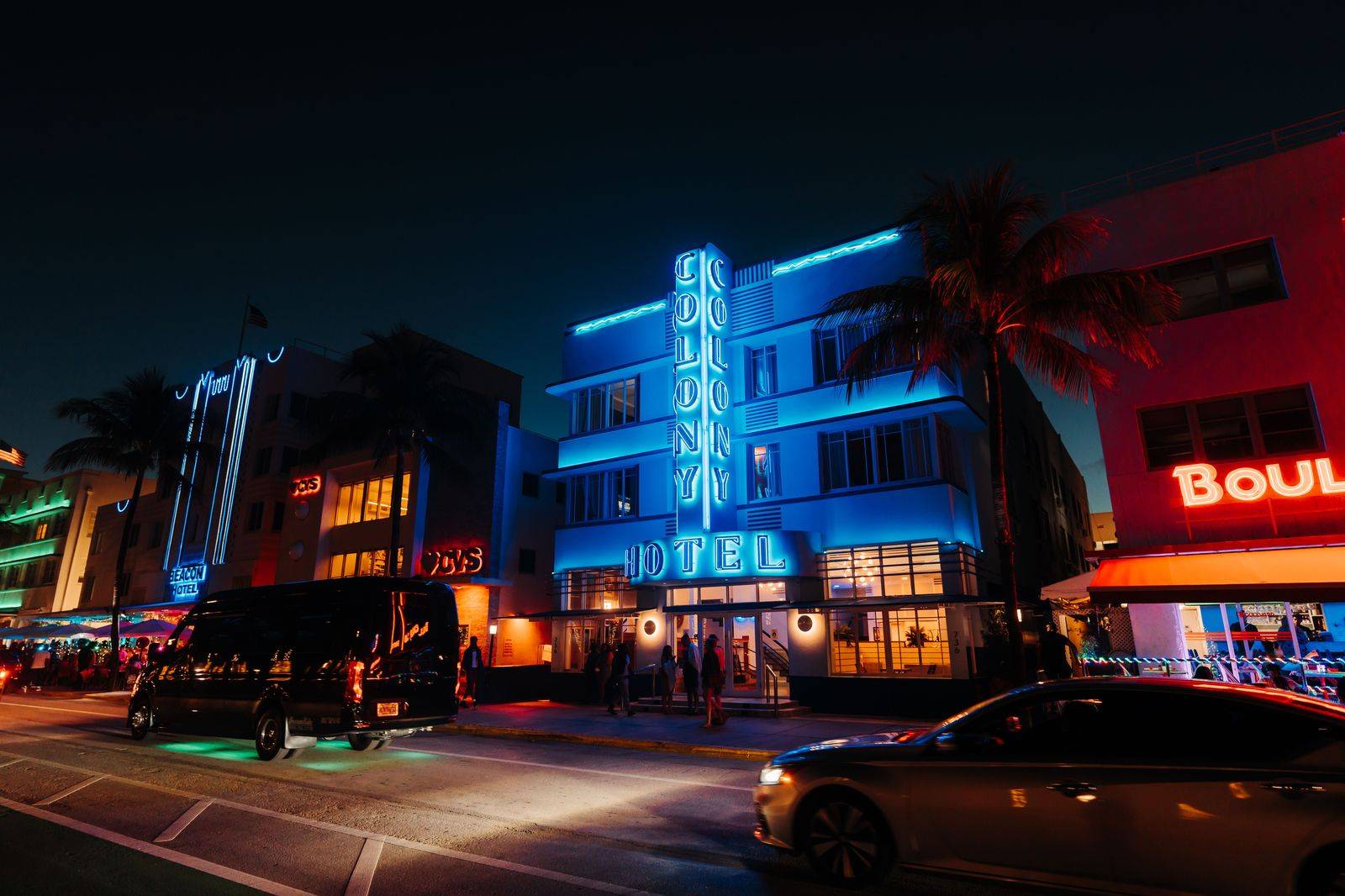 A black sedan waiting under the lights of a hotel entrance at night