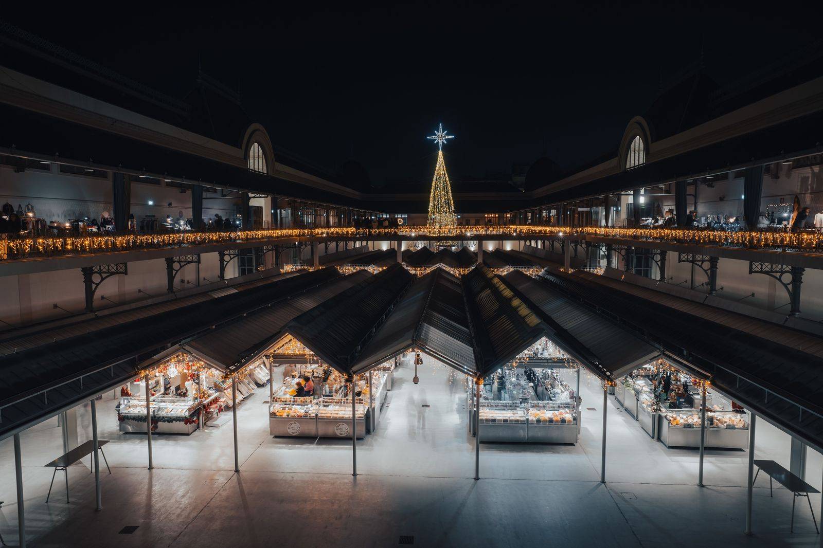 A Christmas market with string lights and crowds in a brick-lined street at night