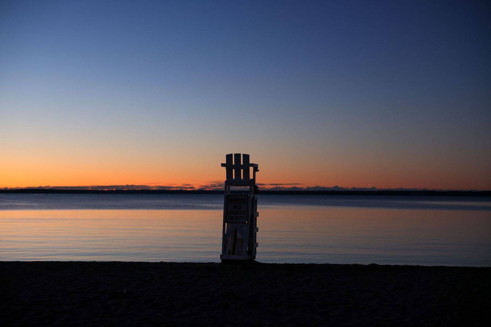 Muskoka chairs on a dock overlooking a calm lake at sunset