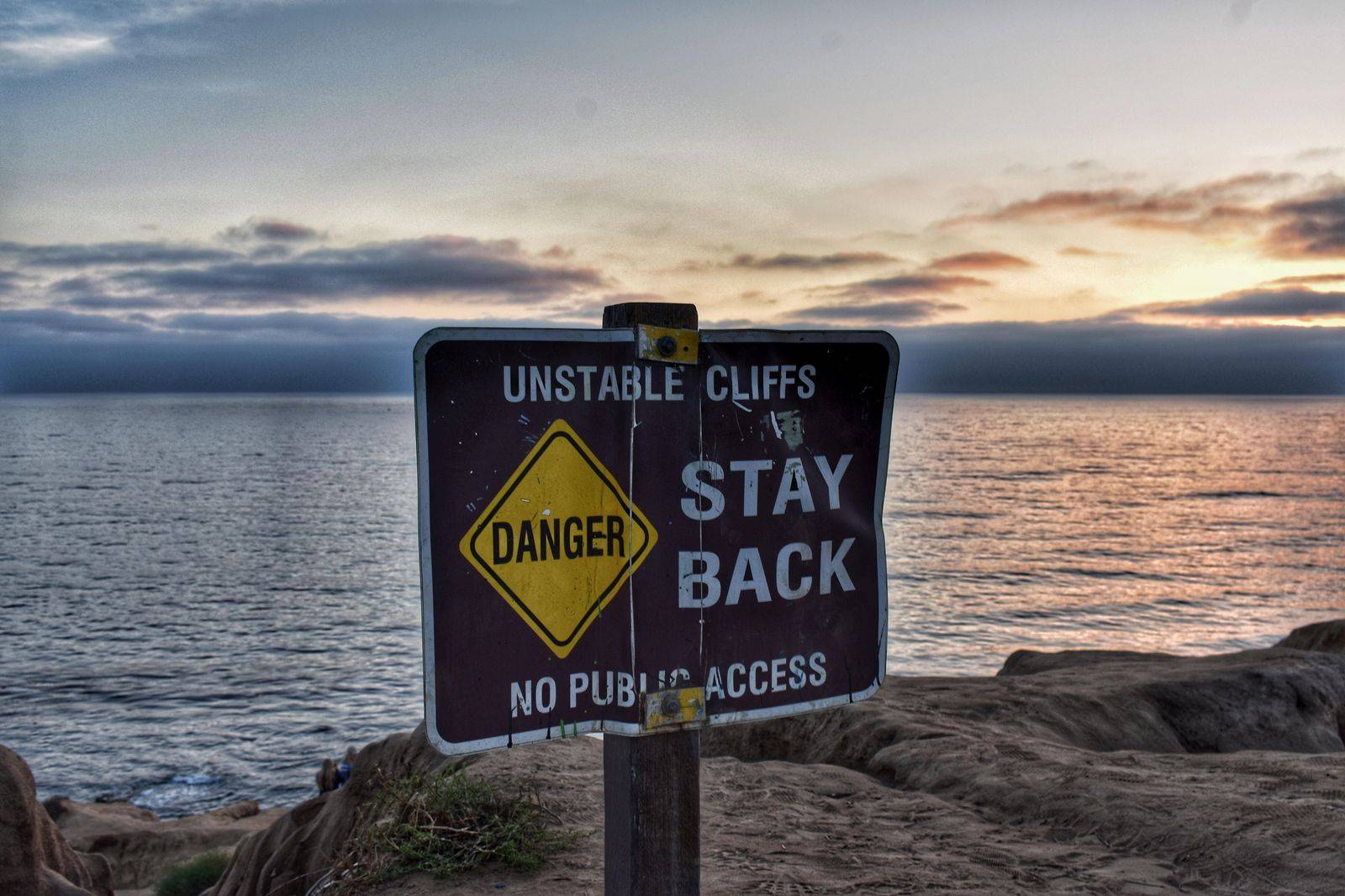 A lakeside trail beneath tall pale cliffs at sunset