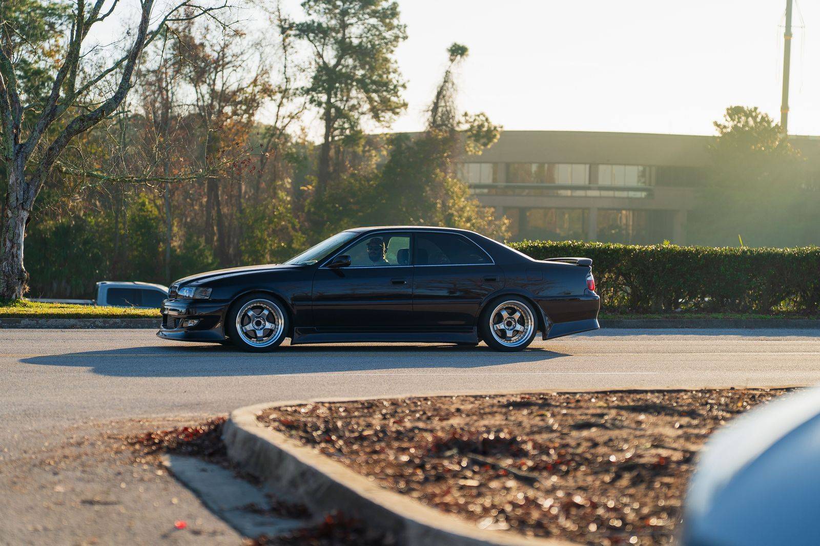 A black sedan waiting on a downtown street, ready to load market bags after a Saturday morning shop
