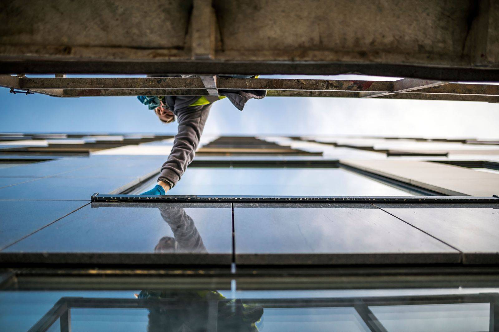 A harnessed walker leaning out from the edge of a tall building high above a city