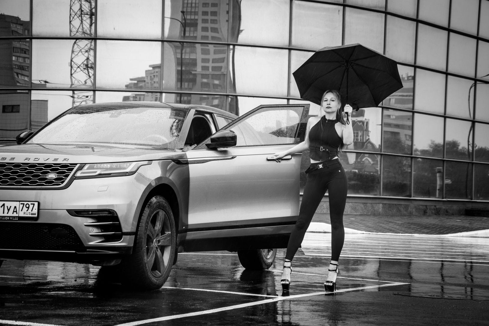 A chauffeur holding an umbrella beside a black car door on a rainy funeral day