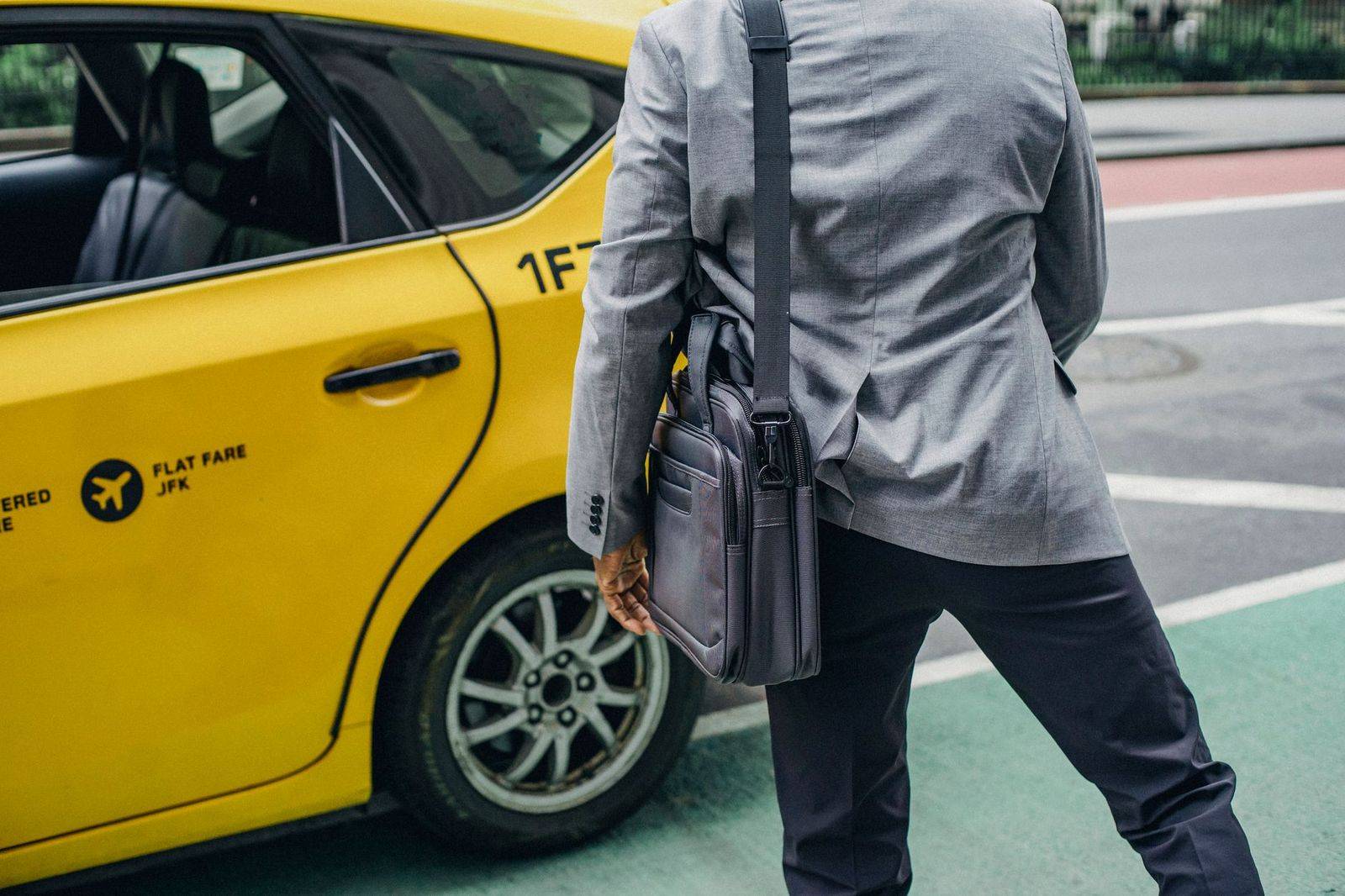 A chauffeur opening the rear door of a black sedan on a downtown side street