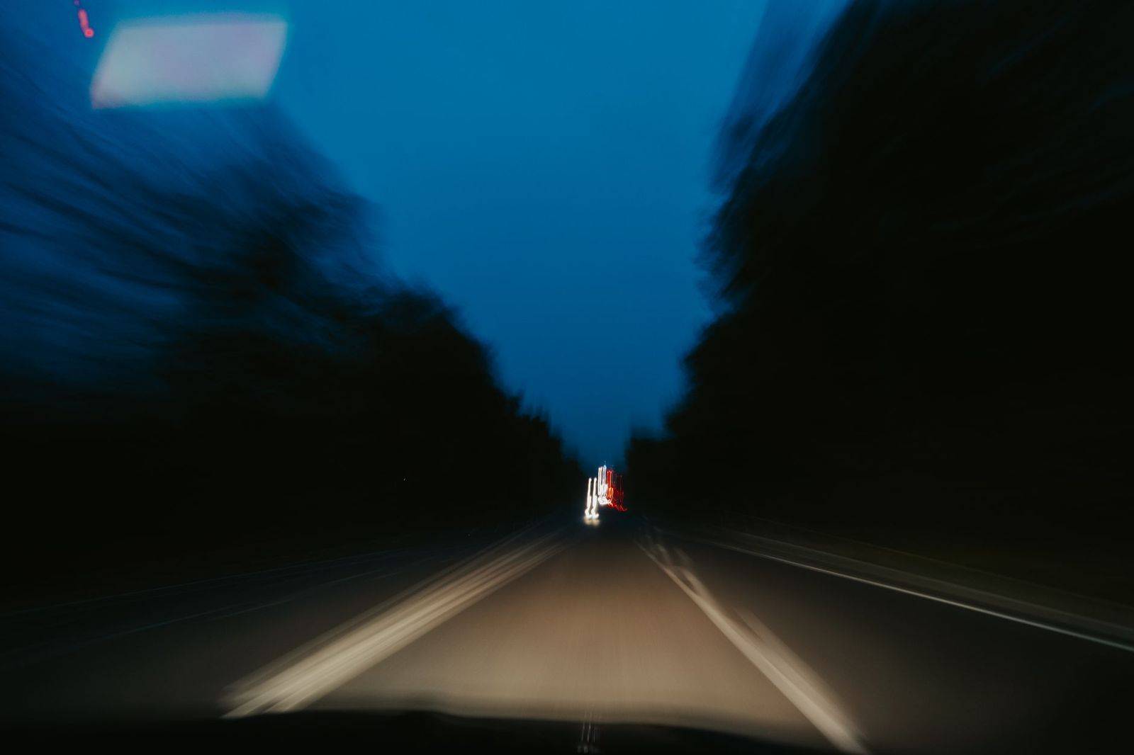 Car headlights on a highway through dark forest at dusk heading north