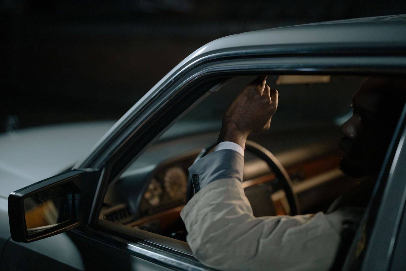 A chauffeur waiting beside a black sedan on a quiet side street after a show