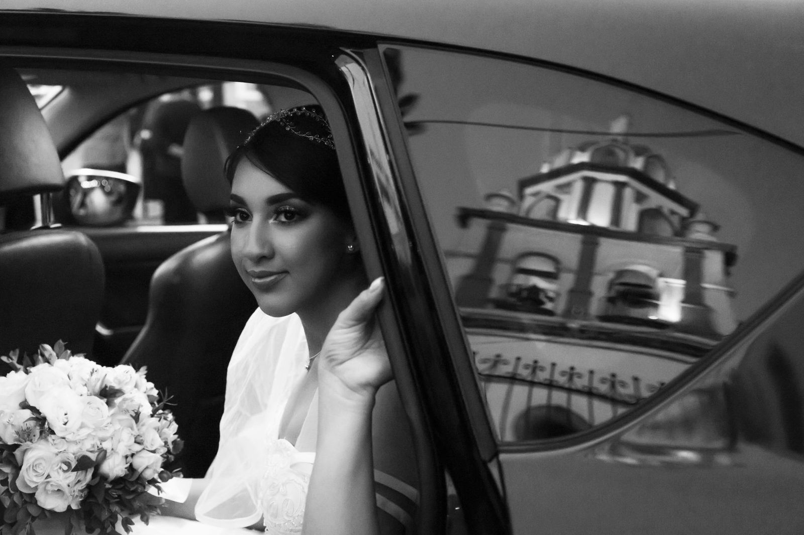 A bride steps out of a luxury wedding car while the chauffeur holds the rear door