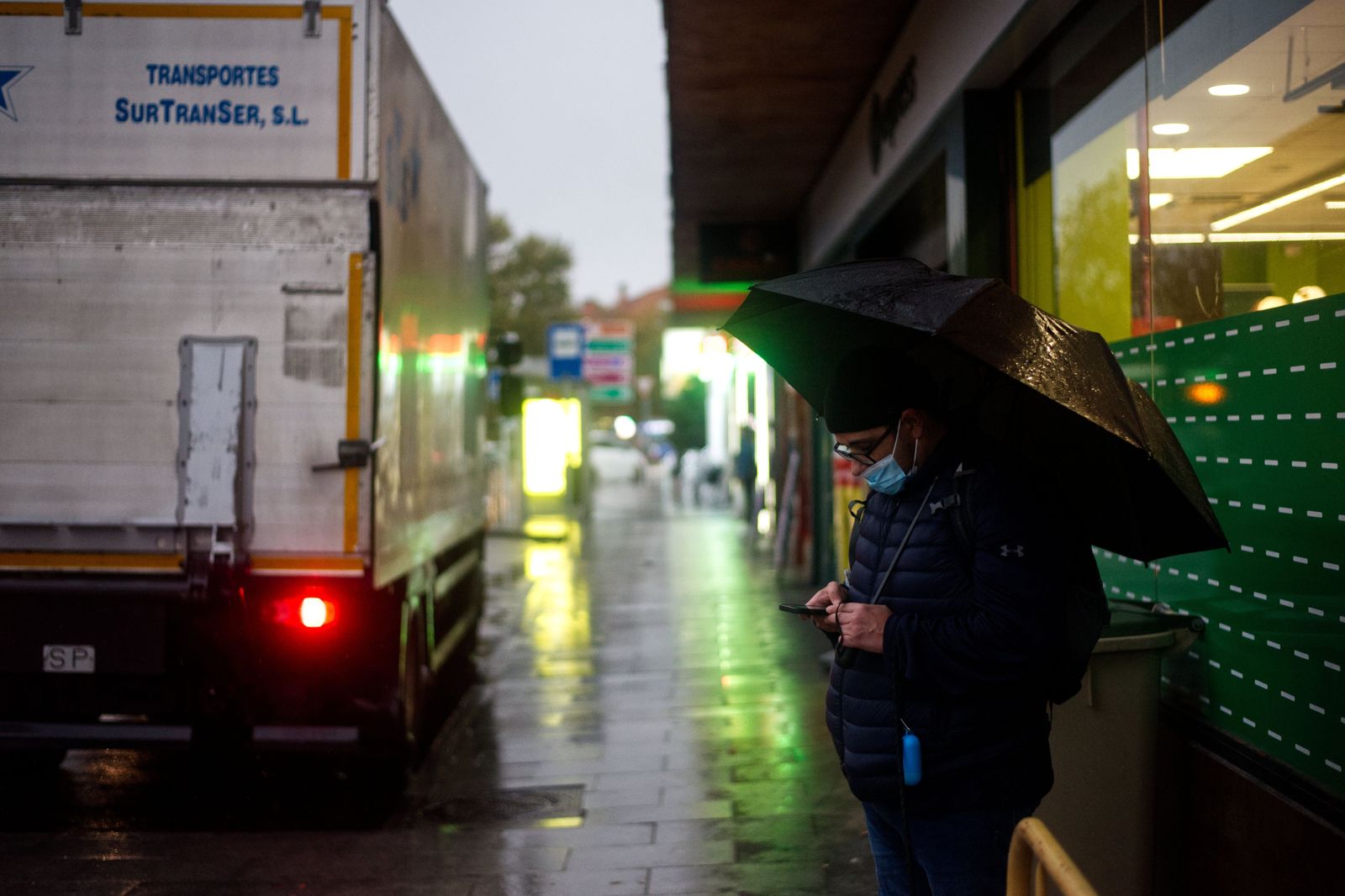 A passenger waiting at a wet Toronto curb for a ride-hail car to arrive
