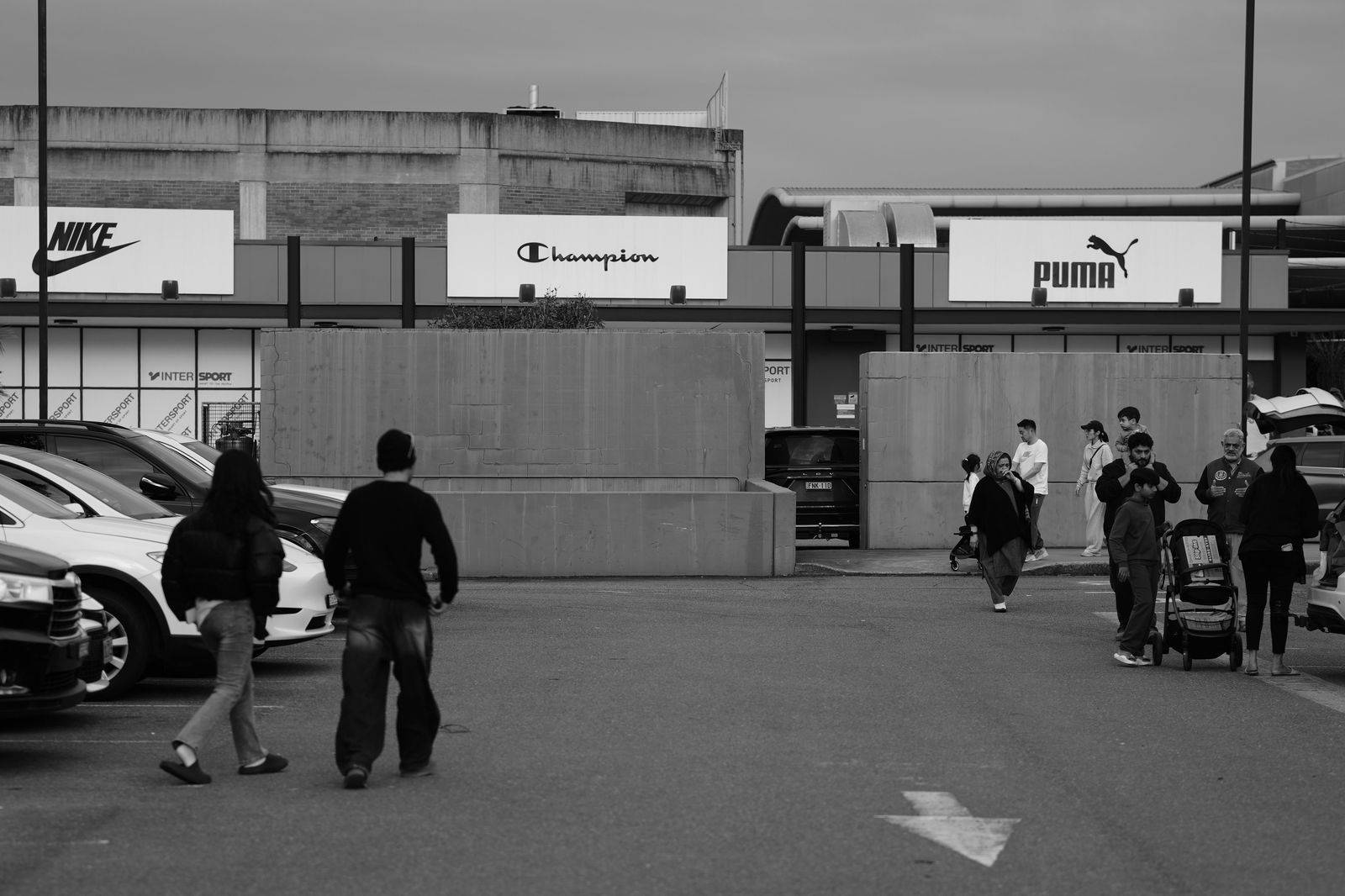 A family walking across a large shopping-centre parking lot toward the entrance