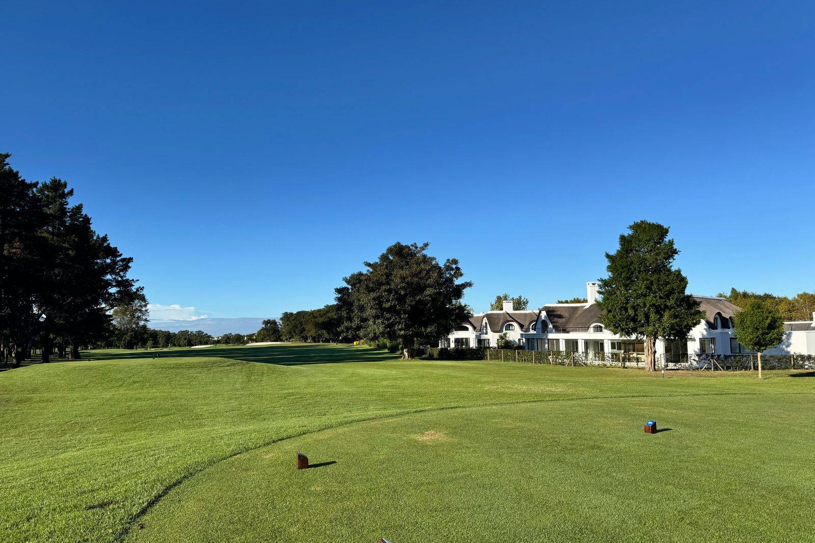 A golf clubhouse in morning light, where a chauffeur waits through the round