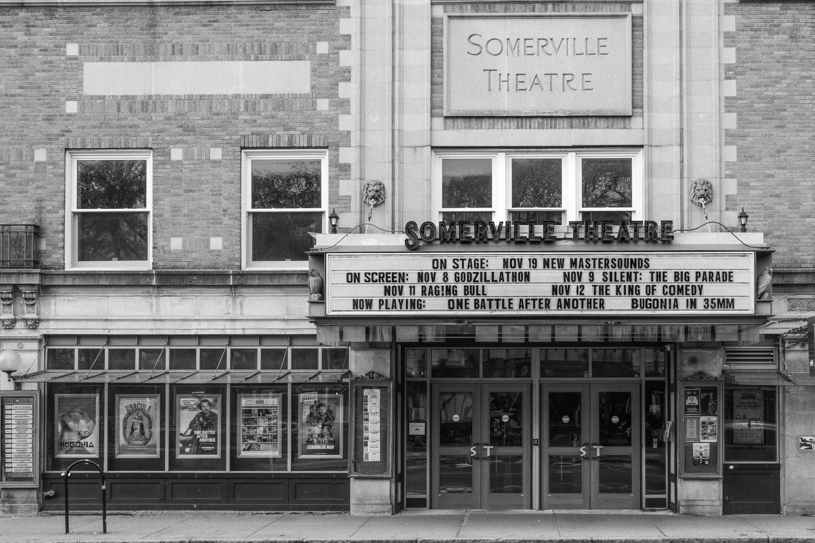 A black sedan waiting outside a theatre entrance in the evening