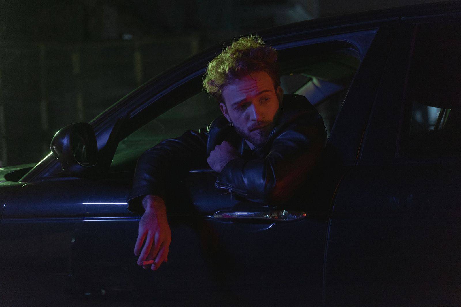A chauffeur holds the rear door of a black sedan outside a restaurant at night