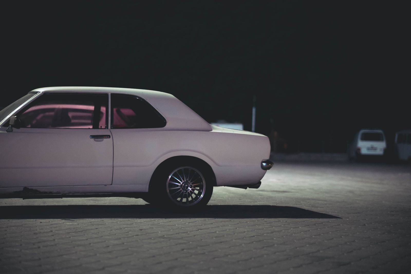 Chauffeur holding the rear door of a black car on a downtown street at night
