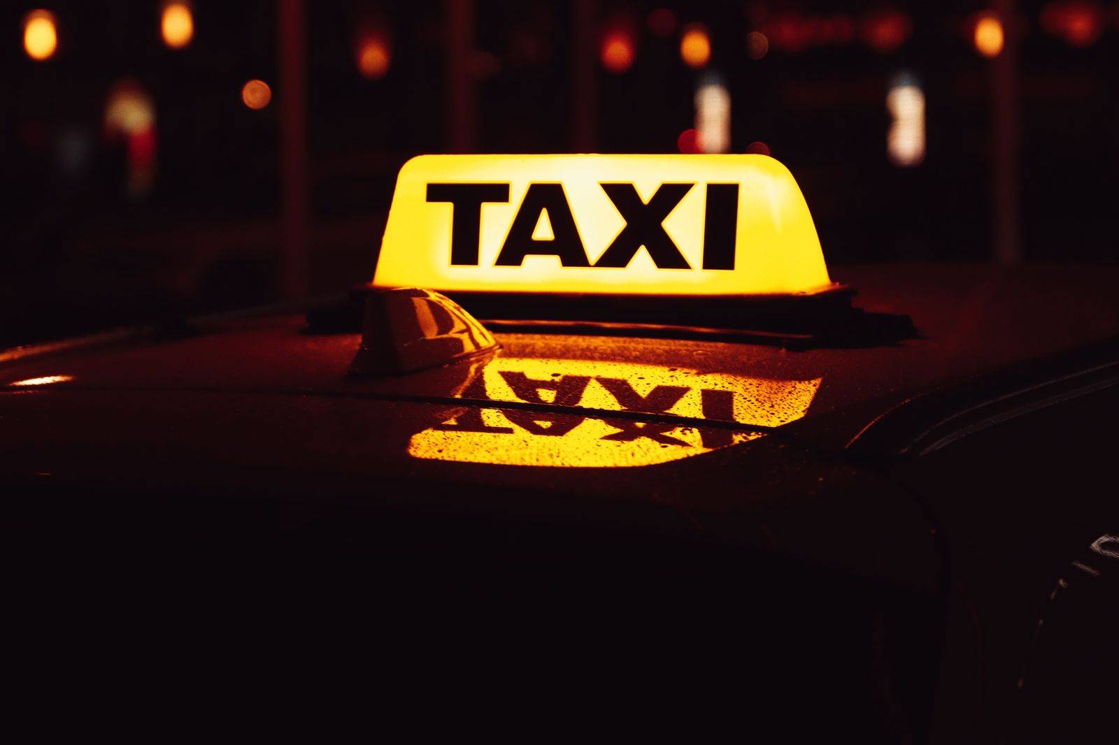Black sedan pulling up at an airport curb at night to collect an arriving passenger