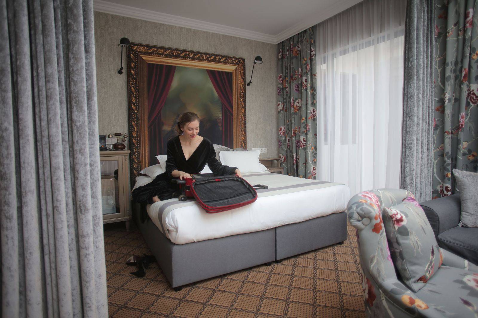 A traveller with a suitcase at a hotel curb as a car arrives in the morning