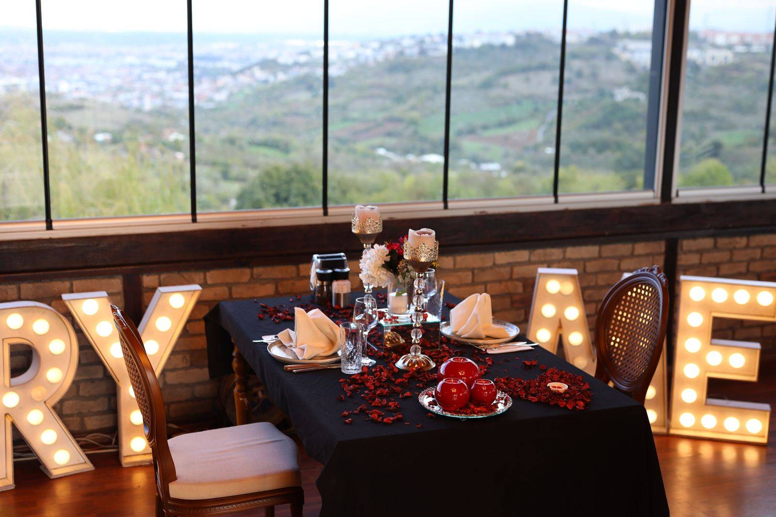 A table set for two with city lights beyond the window, the centrepiece of a chauffeured anniversary evening