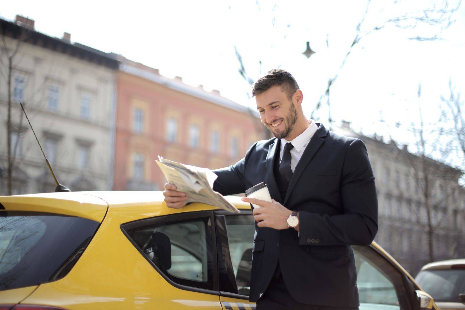 A Toronto livery chauffeur in a dark suit waiting beside an unmarked black car