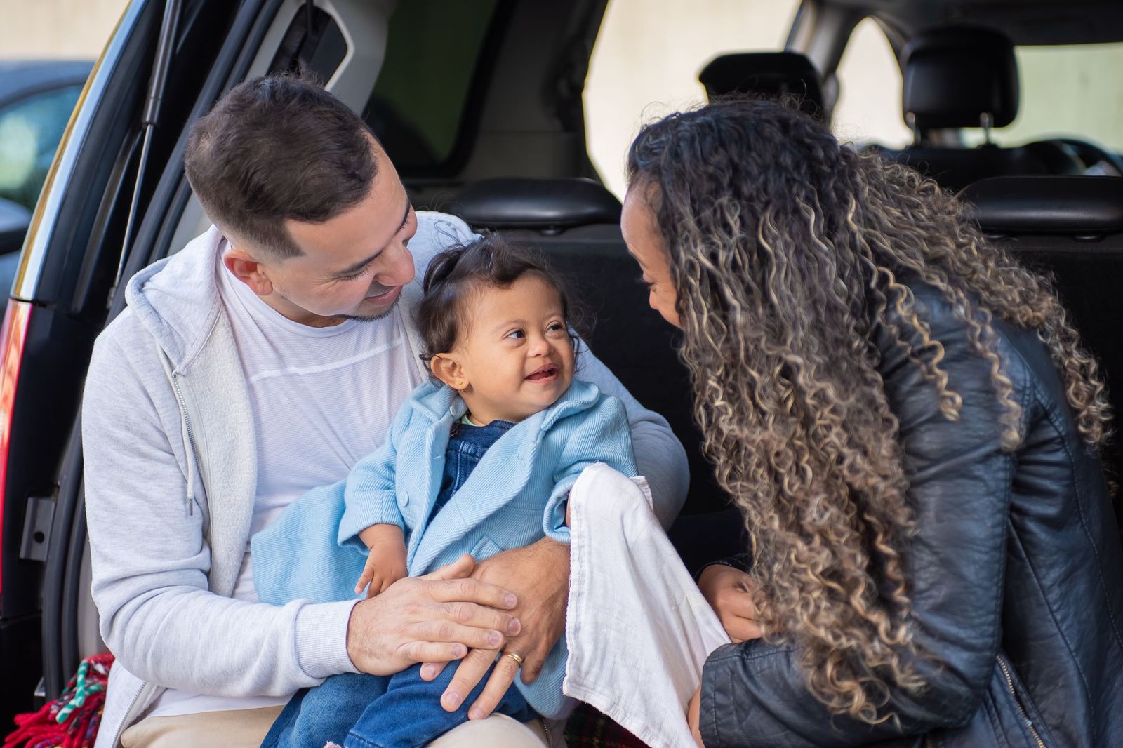 Parents settling their toddler at the back of the car before a family trip