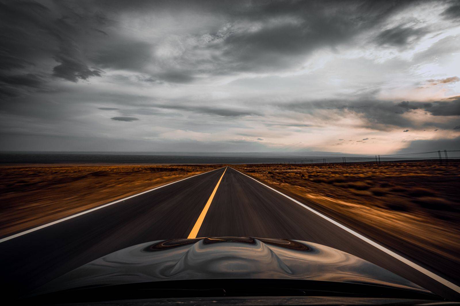A black car on a long, flat stretch of highway through southwestern Ontario farmland