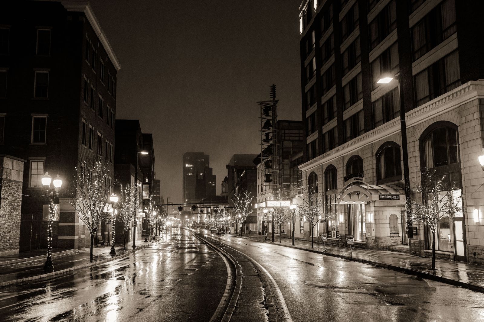 A black sedan on a wet downtown street at night with city lights reflected